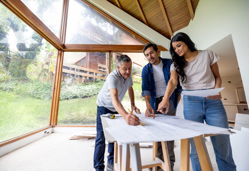 In Annapolis, MD, three people review blueprints at a table, planning a home renovation project.